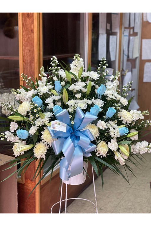 White and blue funeral floor basket featuring roses, lilies, and carnations, handcrafted by a Brooklyn florist for a serene and heartfelt tribute.